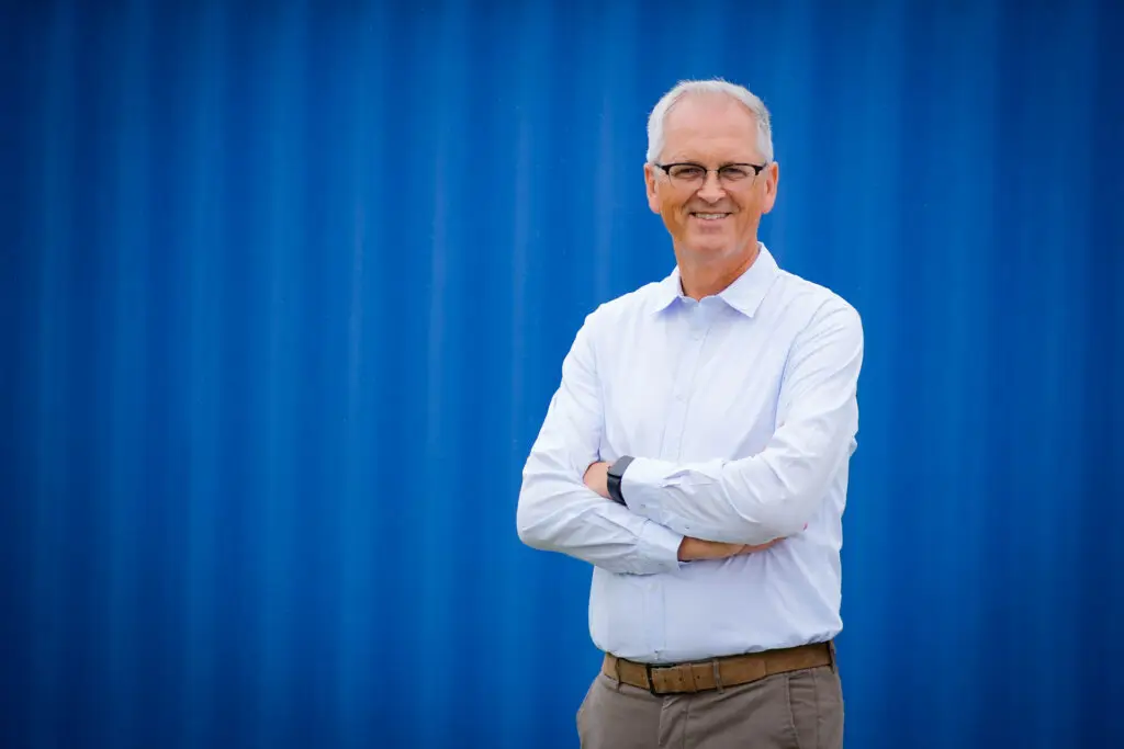 Hinrich Wendroth mit verschränkten Armen vor einer blauen Containerwand